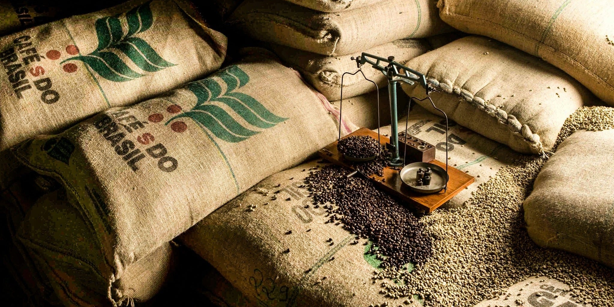 Coffee sacks and a balance scale surrounded by green and roasted coffee beans